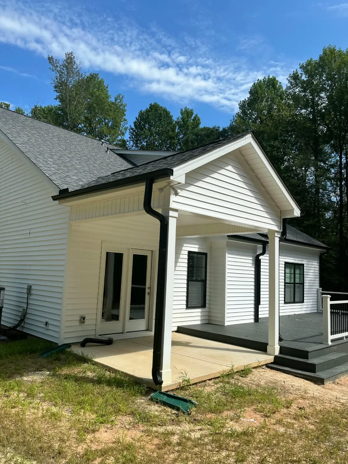White house with a new covered porch, shingle roof and black gutters